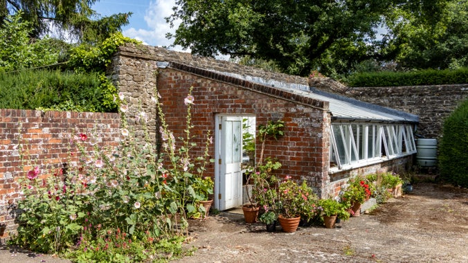 Front view of a greenhouse made of brick and glass from Munstead Wood in Surrey